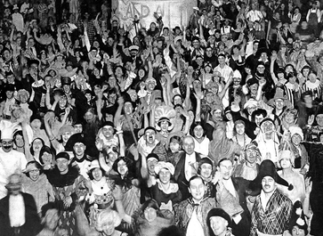 Hundreds of people in all kinds of dress smiling and holding their arms up to the camera.