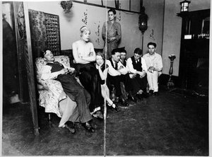 Eight people seated, one standing, in a room looking at the camera.